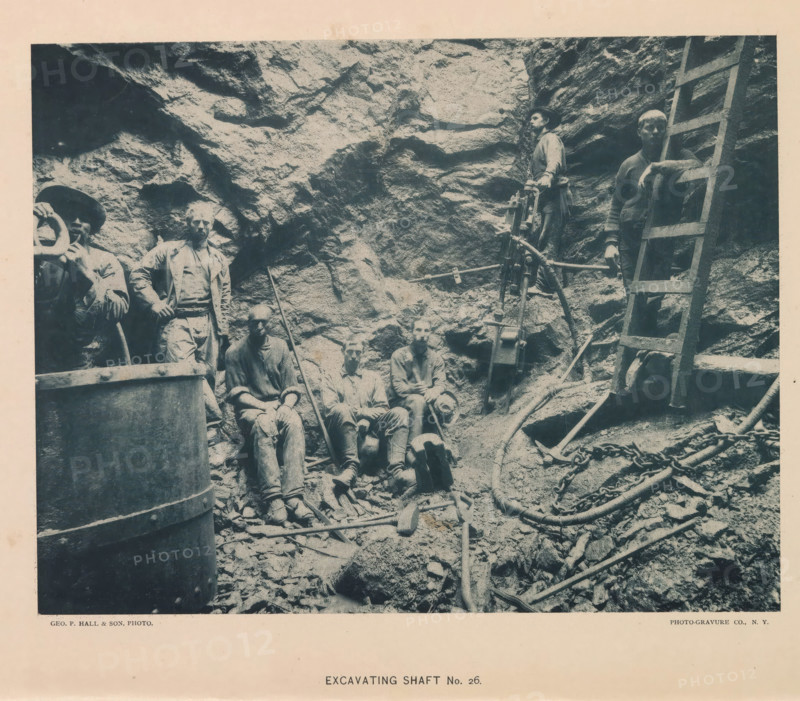Excavating shaft No. 26, page, photomechanical print, photographer: Hall & Son, George P., New York, cliché maker: The Photo-gravure Co., c. 1883 - in or before 1887, North America, paper, collotype, photoprint, height 352 mm x width 281 mm, Print on frontispiece., working class, labourers, digging (industrial process), shafts and galleries (of a mine), A sepia-toned photograph shows a rocky excavation with a rough rock wall as the background and a group of workers standing and sitting on rubble in the foreground, some wearing hats and work clothes and some with tool marks and dirt on their faces and hands; a wooden ladder leans against the rock on the right side and a tripod-mounted mechanical drill or hoisting device stands near the center, surrounded by chains, hoses, and scattered hand tools resting on the ground and on rocks.