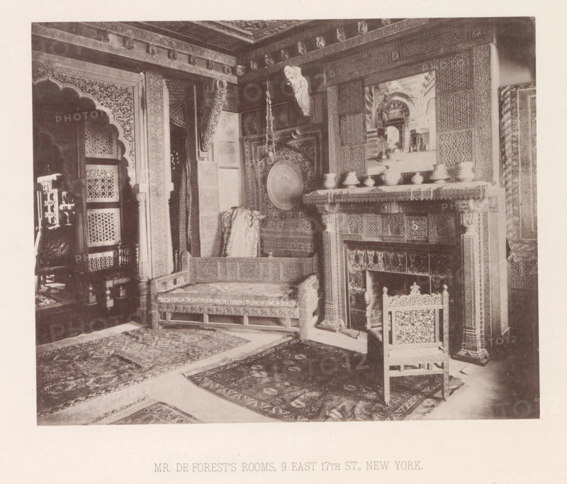 Interior of the house of Lockwood de Forest in New York, page, photomechanical print, title: 'MR. DE FOREST'S ROOMS, 9 EAST 17TH ST., NEW YORK.', number: 'XX.', New York (city), maker: Heliotype Printing Company, Boston (Massachusetts), c. 1875 - in or before 1885, Heliotype Printing Company, photographer, North America, Massachusetts, paper, photoaquatint, height 185 mm x width 232 mm, interior of the house, decorations (interior of the house), An interior view of a richly decorated room showing carved wooden architectural details, patterned wall panels, and ornate moldings along the ceiling; a carved wooden bed or daybed with patterned upholstery and a draped textile rests against a wall; a circular metal tray or gong hangs on the wall above the bed with a long decorative chain suspended nearby; a carved fireplace surround with intricate panels and a mantel holds a row of small vessels and a framed scene depicting an arched architectural opening; a carved wooden chair with an openwor...