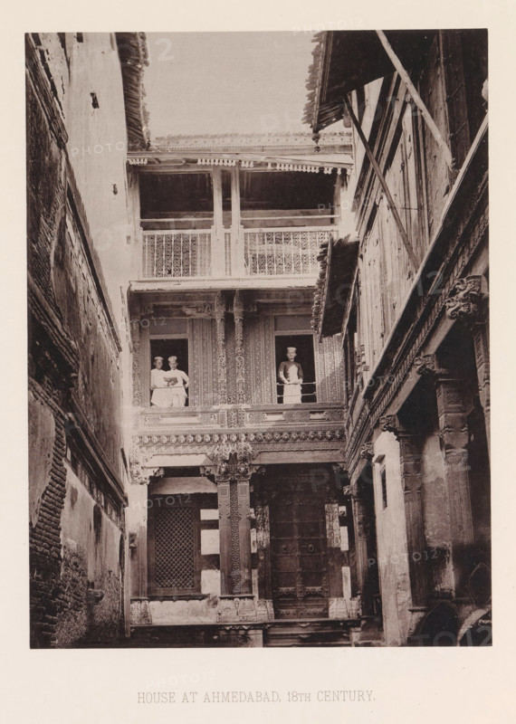 View of a house with three men in Ahmedabad, Gujarat, India, page, photomechanical print, number: 'III.', title: 'HOUSE AT AHMEDABAD, 18TH CENTURY.', Ahmedabad (city), maker: Heliotype Printing Company, Boston (Massachusetts), c. 1875 - in or before 1885, photographer, North America, Massachusetts, paper, photoaquatint, height 233 mm x width 174 mm, urban housing, facade (of house or building), A narrow courtyard framed by tall, ornate walls and balconies, showing intricately carved wooden columns and decorative latticework; three people stand at the upper level, two grouped together at one opening and one at a separate opening, all leaning on the balcony railings; the facade displays patterned panels, carved brackets, and a large central doorway with a grid-covered window beside it; the opposite side shows layered wooden beams and supports with visible wear and textured walls.
