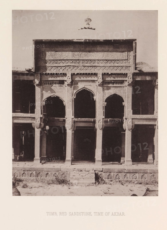 View of a tomb in India from the time of Emperor Akbar, India, page, photomechanical print, title: 'TOMB, RED SANDSTONE, TIME OF AKBAR.', number: 'VII.', maker: Heliotype Printing Company, Boston (Massachusetts), c. 1875 - in or before 1885, photographer, North America, Massachusetts, paper, photoaquatint, height 222 mm x width 175 mm, grave, tomb, A sepia-toned photograph of a building façade showing an ornate upper panel with carved geometric and floral patterns and a cornice, below which are three arched openings framed by decorative columns and carved brackets, a pair of engaged pillars flanking each arch, dark recessed interior spaces visible through the arches, a patterned plinth running along the base with circular medallion motifs, a short central flight of stone steps leading up to the entrance level, patches of vegetation and rough ground in front of the structure, and a light border surrounding the image.