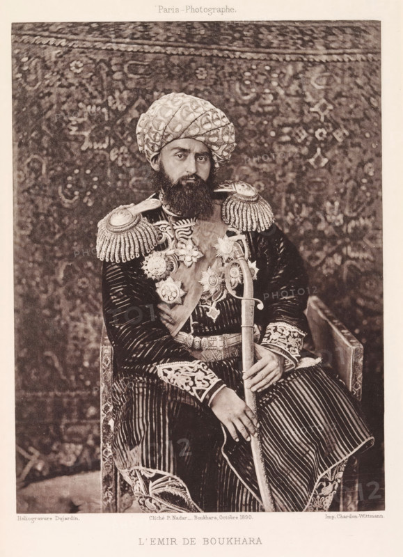 l'Emir de Bukhara, Portrait of the Emir of Bukhara, page, photomechanical print, photographer: Paul Nadar, Bukhara, cliché maker: Dujardin, France, printer (person): Chardon-Wittmann, 1890-10, Paul Nadar, Dujardin, Chardon-Wittmann, photographer, cliché maker, printer (person), Emirate of Bukhara, paper, photoaquatint, height 176 mm x width 132 mm, ruler, sovereign, head-gear: turban, A seated man wearing a patterned turban and a full beard looks toward the camera while dressed in a richly decorated uniform with ornate shoulder epaulettes, embroidered cuffs, and a sash adorned with multiple large star-shaped medals; he holds a long curved sword with one hand resting on its hilt and the other on his knee, and a patterned textile backdrop fills the space behind him.
