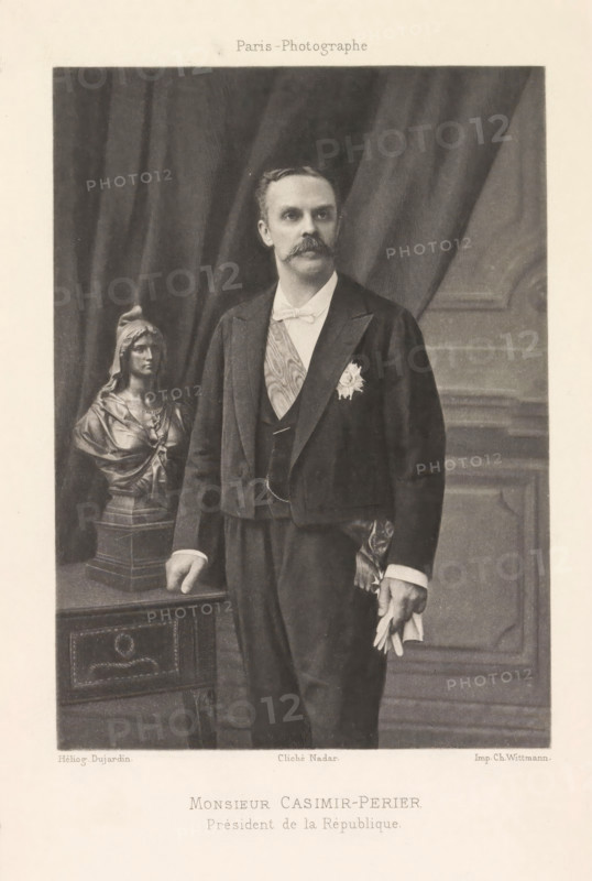 Portrait of Jean Casimir-Perier, Monsieur Casimir-Perier. Prèsident de la République, page, photomechanical print, photographer: Félix Nadar, Paris, cliché maker: Dujardin, France, printer (person): Charles Wittmann, c. 1884 - in or before 1894, printer (person), paper, photoaquatint, height 146 mm x width 105 mm, Person, Jean Casimir-Perier, politician, eg party leader, A monochrome portrait of a man standing beside a table with a sculpted bust on it; the man wears a dark formal jacket with a light bow tie and a sash across his chest, a decorative star pinned to his jacket, and holds a pair of gloves in one hand while the other hand rests on the table; behind him are heavy draped curtains and paneled wall details, and the sculpted bust depicts a robed female figure on a square base.