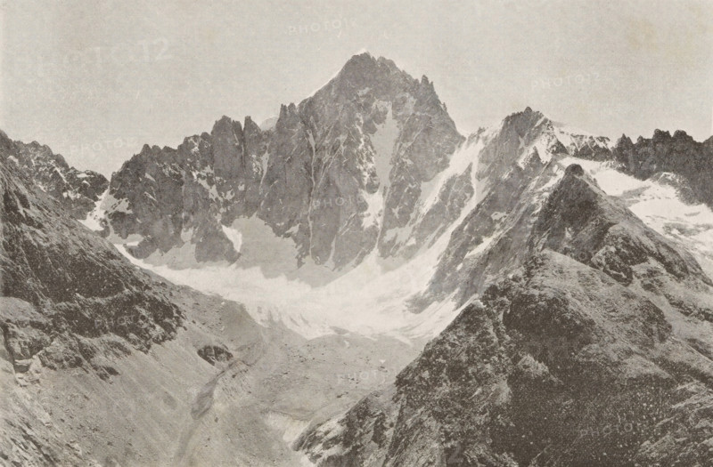 View of the snowy peaks of mountains in Ecrins, Col et dome de neiges des Ecrins, page, photomechanical print, inscription: '(Extrait de l'Echo des Alpes, Geneve.', photographer: ME Courvoisier, c. 1890 - in or before 1895, ME Courvoisier, photographer, paper, autotypie, height 109 mm x width 168 mm, snow, mountains, Écrins, Les, A wide grayscale photograph showing a rugged mountain range with steep jagged peaks and snow-filled gullies, with a prominent central peak rising above surrounding ridges. In the foreground there are rocky slopes and a ridge descending toward a valley floor that appears to be partially covered in snow or ice. The sky above the mountains is clear and light in tone. The image has a textured, grainy appearance.