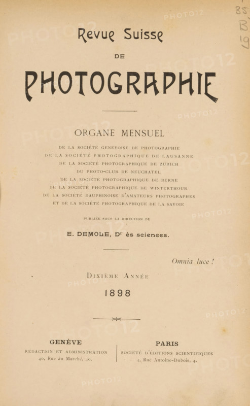 Revue suisse de photographie, Société genevoise de photographie, et al., book, annotation: 'NOV, 1994', number: 'bl. 112, 143', name: 'Jer. Van Severen, Ruysselede', collector's mark: 'Dr. Frans de Vos, 54, Ter Rivierenlaan, DEURNE, Telst.: 5.6.90 - Postcheckr. 504.1..', editor (person who revises): Eugène Demole, 1898, Eugène Demole, editor (person who revises), textile materials, pasteboard, biological material, paper, linen (material), leather, printing, shell marbled paper, agate marbled paper, lithography, autotype, collotype, height 231 mm x width 163 mm x thickness 28 mm, A vertical page with aged beige paper showing large bold stylized lettering near the top, a centered thin horizontal rule below it, and multiple lines of smaller printed lines arranged in centered blocks down the page, with a decorative divider element in the lower-middle area and two wider columns of text near the bottom separated by a thin vertical line, plus small pencil scribbles in the top right margin.