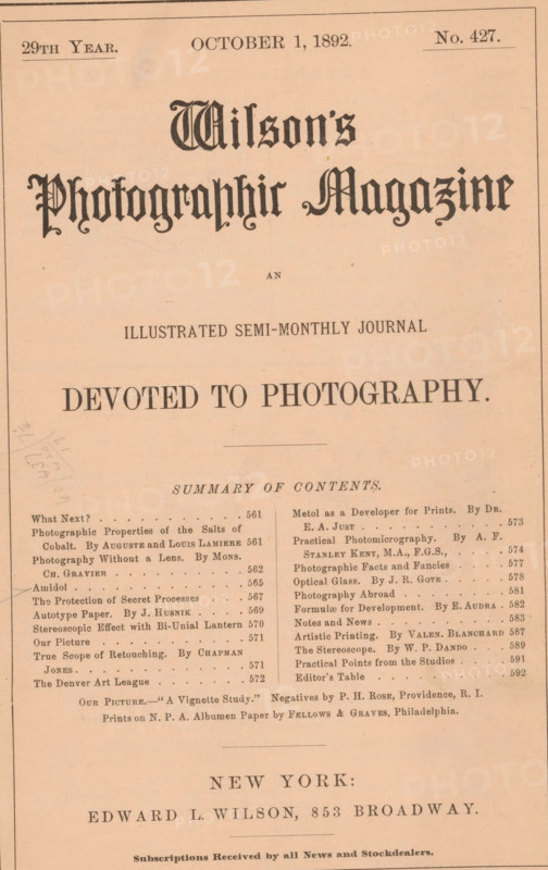 Wilson's photographic magazine, magazine, publisher: Edward Livingston Wilson, New York (city), 1892-10-01, Edward Livingston Wilson, publisher, North America, paper, printing, wood engraving, autotype, albumen print, height 256 mm x width 176 mm x thickness 4 mm, A sepia-toned page showing a magazine cover with a decorative title in a blackletter style centered near the top, a subtitle in a simpler serif font beneath it, a large bold headline in uppercase across the middle, and a horizontal rule below; a two-column list of short entries and headings fills the lower portion with small serif type, and a centered city line and publisher line appear toward the bottom in larger serif capitals; the page has a thin border, some small stains and faint pencil marks on the left, and the overall paper shows age with slight discoloration.
