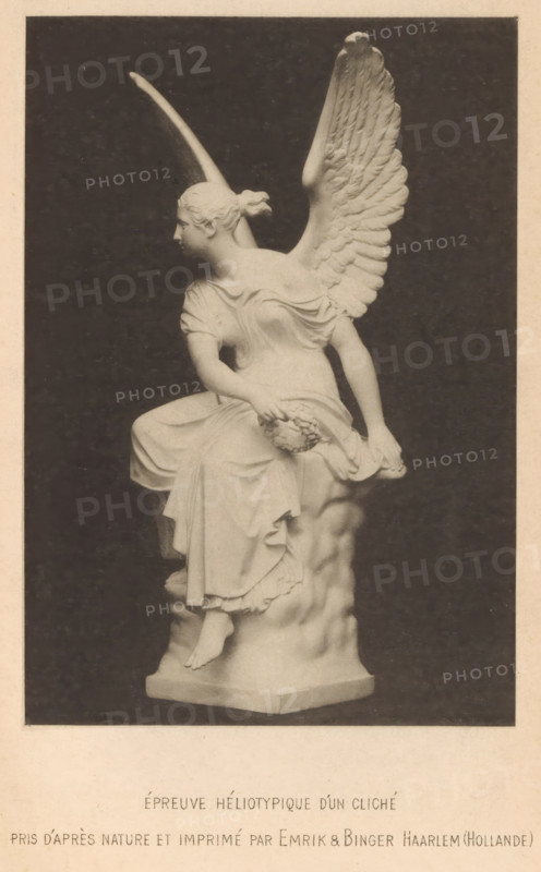 View of a statue of an angel with a wreath in his hand, photograph, page, inscription: 'Épreuve Héliotypique dún cliché, pris dáprès nature et imprimé by Emrik & Binger Haarlem (Hollnde)', cliché maker: anonymous, printer (person): Emrik & Binger, Haarlem, c. 1883 - in or before 1888, photographer, printer (person), paper, collotype, photoprint, height 111 mm x width 72 mm, sculpture, A monochrome photograph of a marble statue depicting a seated winged female figure shown in profile facing left, with hair pulled back into a bun and draped clothing that forms folds over her torso and legs; one arm rests on her knee holding a rounded object while the other hand drapes fabric at her side, and a large detailed wing rises behind her shoulder; the figure sits on a sculpted rocky base with one foot visible on a plinth, set against a dark background and framed by a light border.