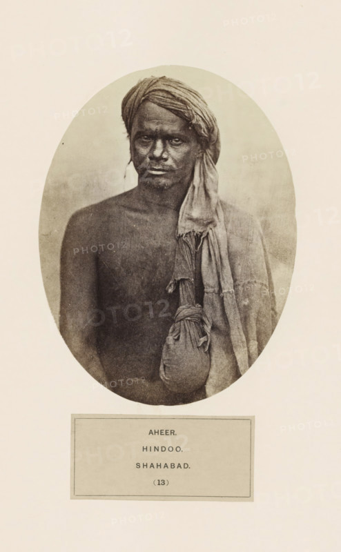 Portrait of an unknown man from the Ahir community of Arrah (former Shahabad) in Bihar, India, photograph, page, inscription: 'AHEER., HINDOO., SHAHABAD.', number: '(13)', Bihar, c. 1858 - in or before 1868, photographer, North India, paper, albumen print, height 160 mm x width 120 mm, human races, peoples, nationalities, An oval-framed sepia portrait of a bare-chested man wearing a wrapped headscarf and a draped cloth over one shoulder, with a tied pouch hanging from the draped cloth; the man's face has a neutral expression and his gaze is directed forward.