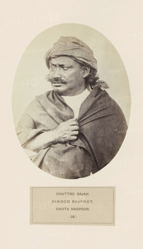 Portrait of the Maharaja of Chota Nagpur, photograph, page, number: '(24)', inscription: 'CHUTTRO RAJAH., HINDOO RAJPOOT., CHOTA NAGPOOR.', photographer: Benjamin Simpson (possibly), Chota Nagpur, c. 1858 - in or before 1868, Jharkhand, paper, albumen print, height 158 mm x width 120 mm, head-gear: turban, human races, peoples, nationalities, A sepia-toned oval portrait of a man shown from the waist up wearing a wrapped headscarf and a draped shawl, looking slightly to his left with a mustache and short beard, one hand gripping the shawl at his chest, set against a plain light background with a rectangular label area below the portrait.