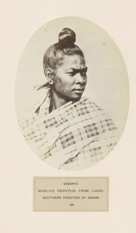 Portrait of an unknown woman from the Singpho tribe of Assam, photograph, page, The tribe is also found in Arunachal Pradesh., number: '(29)', inscription: 'SINGPHO., WARLIKE FRONTIER TRIBE (LAOS)., SOUTHERN FRONTIER OF ASSAM.', photographer: attributed to Benjamin Simpson, Assam, c. 1858 - in or before 1868, Attributed to, paper, albumen print, height 175 mm x width 130 mm, human races, peoples, nationalities, A sepia-toned oval portrait of a person shown from the shoulders up, turned in three-quarter profile to the right, with hair pulled into a top knot and a strand of hair behind the ear, wearing a patterned shawl draped across the shoulders; the portrait is mounted on a pale background with a rectangular label area beneath the oval.