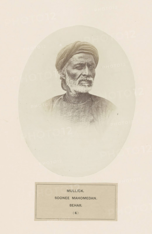 Portrait of an unknown man from the Malik clan of Bihar in eastern India, photograph, page, inscription: 'MULLICK., SOONEE MAHOMEDAN., BEHAR.', number: '(4)', Bihar, c. 1858 - in or before 1868, photographer, North India, paper, albumen print, height 158 mm x width 121 mm, human races, peoples, nationalities, A sepia-toned oval portrait of an older man with a turban and a trimmed white beard, shown from the shoulders up and turned slightly to one side, wearing a textured garment, centered on a pale background with a rectangular plaque visible beneath the oval.
