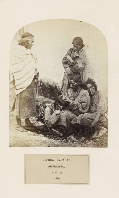 Five unknown men on the street from the Lepcha community of Sikkim, photograph, page, number: '(49)', inscription: 'LEPCHA PEASANTS., ABORIGINAL., SIKHIM.', photographer: Benjamin Simpson (possibly), Sikkim, c. 1858 - in or before 1868, paper, albumen print, height 167 mm x width 129 mm, street, human races, peoples, nationalities, A sepia-toned photograph framed within an arched top shows a group of five people clustered near a light-colored wall, with one person standing at the left wrapped in a striped shawl and holding a long staff, two seated figures leaning against each other on the right, one seated central figure gently touching the head of a smaller seated person who rests against them, and another person standing behind with arms crossed and head bowed; the ground beneath them is uneven and textured, their clothing appears layered and worn, and the overall scene has a soft, aged photographic quality.