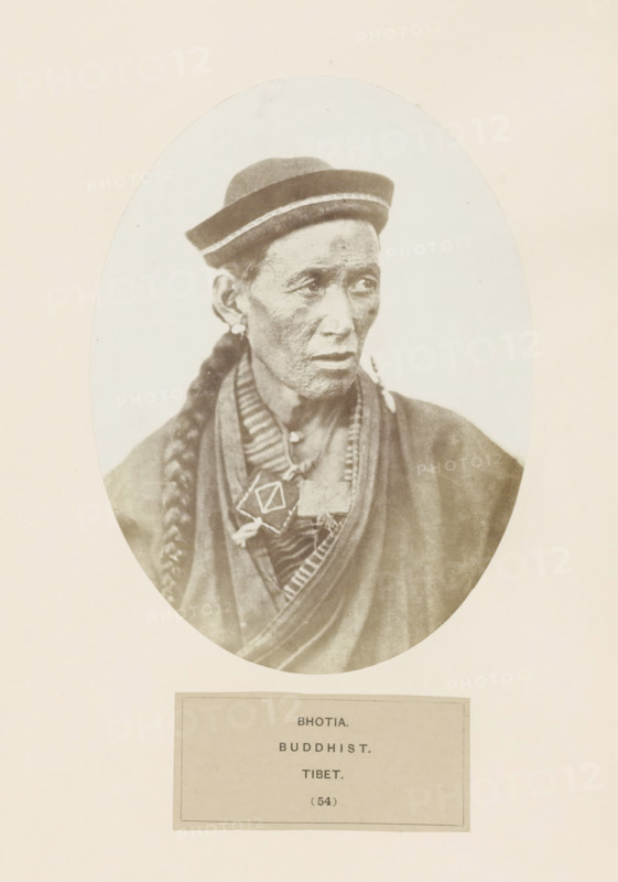 Portrait of an unknown man from the Bhutia community of Tibet, photograph, page, inscription: 'BHOTIA., BUDDHIST., TIBET.', number: '(54)', photographer: Benjamin Simpson (possibly), Tibet, c. 1858 - in or before 1868, paper, albumen print, height 175 mm x width 130 mm, Hinduism, Buddhism, Jainism, human races, peoples, nationalities, An oval sepia portrait of an older person shown from the chest up wearing a brimmed hat with a light band, a long braided hairstyle draped over one shoulder, earrings, layered robes and necklaces with a geometric pendant, and a neutral facial expression with visible skin texture, all set against a light background within a rectangular page.