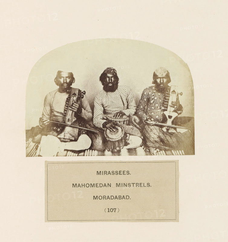 Portrait of three unknown minstrels from Moradabad, Uttar Pradesh, India, photograph, page, inscription: 'MIRASSEES., MAHOMEDAN MINSTRELS., MORADABAD.', number: '(107)', Moradabad, c. 1858 - in or before 1868, photographer, North India, paper, albumen print, height 75 mm x width 107 mm, minstrel, 'juggler', human races, peoples, nationalities, A sepia photograph shows three seated men in traditional clothing, each with a beard and head covering, positioned side by side; the man on the left holds a bowed string instrument across his lap, the man in the center rests his hands on a drum placed between his knees, and the man on the right holds a plucked instrument with a long neck; patterned fabrics and striped textiles are visible beneath them and their garments feature varied prints and textures.
