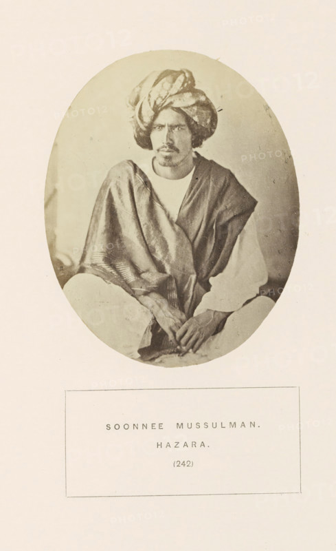 Portrait of an unknown man with a turban from the Yusufzai Pathan tribe of Hazara, Khyber Pakhtunkhwa, Pakistan, photograph, page, inscription: 'SOONNEE MUSSULMAN., HAZARA.', number: '(242)', Hazara, c. 1862 - in or before 1872, photographer, paper, albumen print, height 106 mm x width 86 mm, head-gear: turban, human races, peoples, nationalities, An oval sepia photograph shows a seated man wearing a turban and draped garments, his face framed by the turban and a short mustache and beard, with his hands resting in his lap and his gaze directed slightly to the side; the oval image is set against a plain light background and mounted above a rectangular area that contains printed content.