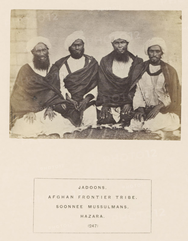 Portrait of four unknown men from the Jadoon tribe of Hazara, Khyber-Pakhtunkhwa, Pakistan, photograph, page, number: '(247)', inscription: 'JADOONS., AFGHAN FRONTIER TRIBE., SOONNEE MUSSULMANS., HAZARA.', Hazara, c. 1862 - in or before 1872, photographer, paper, albumen print, height 86 mm x width 115 mm, human races, peoples, nationalities, A sepia-toned photograph shows four seated men wearing turbans and draped garments, each with visible beards and hands resting on their laps; the men sit closely together on a patterned surface against a plain backdrop, and the image has a faded, aged appearance with light borders around it.