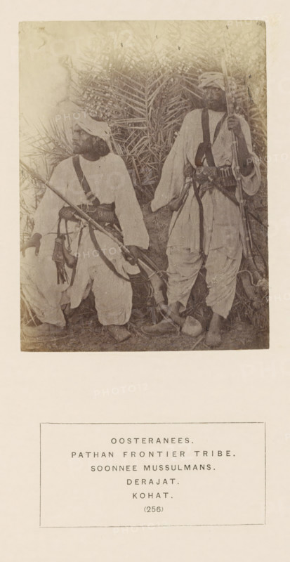 Portrait of two unknown men with muskets from the Storyani tribe of Kohat, Khyber Pakhtunkhwa, Pakistan, photograph, page, The Storyani tribe is also known as Ustrani., number: '(256)', inscription, q: 'EASTERNEESE., PATHAN FRONTIER TRIBE., SOONNEE MUSSULMANS., DERAJAT., KOHAT.', Kohat, c. 1862 - in or before 1872, photographer, paper, albumen print, height 115 mm x width 87 mm, head-gear: turban, firearms: rifle, human races, peoples, nationalities, A faded sepia photograph shows two men wearing loose traditional garments and turbans standing in front of dense palm fronds; both men carry long rifles and have wide belts with pouches and straps across their chests, one man standing slightly behind the other while the other rests a hand on his knee, and the ground around their feet is covered with grass and a rounded object.
