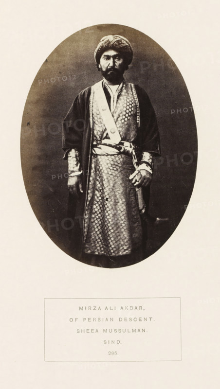 Portrait of Mirza Ali Akbar, a nobleman of Persian descent, Sindh, Pakistan, photograph, page, inscription: 'MIRZA ALI AKBAR, OF PERSIAN DESCENT., SHEEA MUSSULMAN., SIND.', number: '295.', photographer: Henry Charles Baskerville Tanner (possibly), c. 1862 - in or before 1872, paper, albumen print, height 139 mm x width 100 mm, head-gear: turban, prince, human races, peoples, nationalities, An oval sepia photograph shows a standing man facing forward wearing a patterned long robe with a sash and a darker outer coat, a turban on his head, and a mustache and beard; his left hand rests near a sheathed sword at his waist while his right arm hangs by his side, and the oval image is centered on a light background with a rectangular bordered area below containing printed lines.