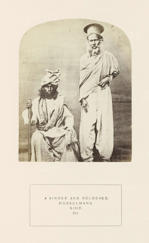 Portrait of two unknown men from Sindhi and Baluch origin in Sindh, Pakistan, photograph, page, Left: a man from a Baloch tribe, right: a man of Sindhi origin., inscription: 'A SINDEE AND BELOCHEE., MUSSULMANS., SIND.', number: '311.', photographer: Henry Charles Baskerville Tanner (possibly), Sindh, photographer: William Robert Houghton (possibly), c. 1862 - in or before 1872, paper, albumen print, height 123 mm x width 96 mm, head-gear: hat, head-gear: turban, human races, peoples, nationalities, A sepia-toned photograph shows two men in traditional clothing framed within a rounded-arch vignette. One man sits, wearing layered draped garments and a turban, holding a long staff with one hand and resting the other on his knee, his face partly shadowed by his hair and beard. The second man stands beside him, wrapped in a loose draped robe with one hand resting near his waist and the other hanging by his side, and he wears a tall cylindrical hat and a long beard. The background is plain a...