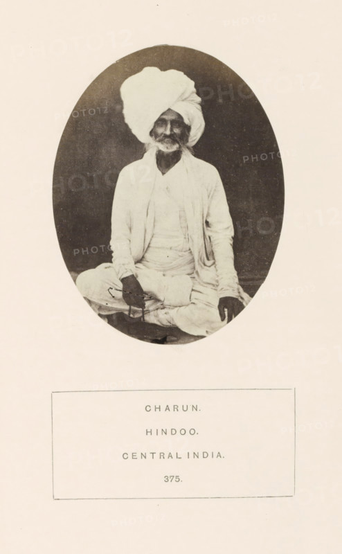 Portrait of an unknown man from the Charan community with a turban, Madhya Pradesh, India, photograph, page, inscription: 'CHARUN., HINDOO., CENTRAL INDIA.', number: '375.', photographer: James John Waterhouse (possibly), 1862, paper, albumen print, albumendruk, height 95 mm x width 74 mm, head-gear: turban, religious functions, Hinduism, Buddhism, Jainism, human races, peoples, nationalities, An oval-framed sepia photograph shows an elderly man seated cross-legged wearing a large wrapped turban and loose light-colored garments, with a long beard and mustache, his hands resting on his knees and a string of beads visible in one hand, set against a dark background and mounted on a pale page with a bordered label beneath the portrait.