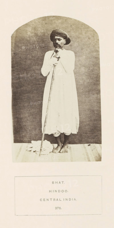Portrait of an unknown man from the Bhat community with a rod, Madhya Pradesh, India, photograph, page, inscription: 'BHAT., HINDOO., CENTRAL INDIA.', number: '376.', photographer: James John Waterhouse (possibly), 1862, Central India, paper, albumen print, height 129 mm x width 79 mm, human races, peoples, nationalities, walking-stick, staff, A monochrome photograph of a barefoot man standing on a mat against a plain arched backdrop, wearing a long light-colored robe and a turban, holding a long staff vertically with both hands near his chest, with a folded cloth on the floor beside the staff and the man's feet visible at the hem of his robe.