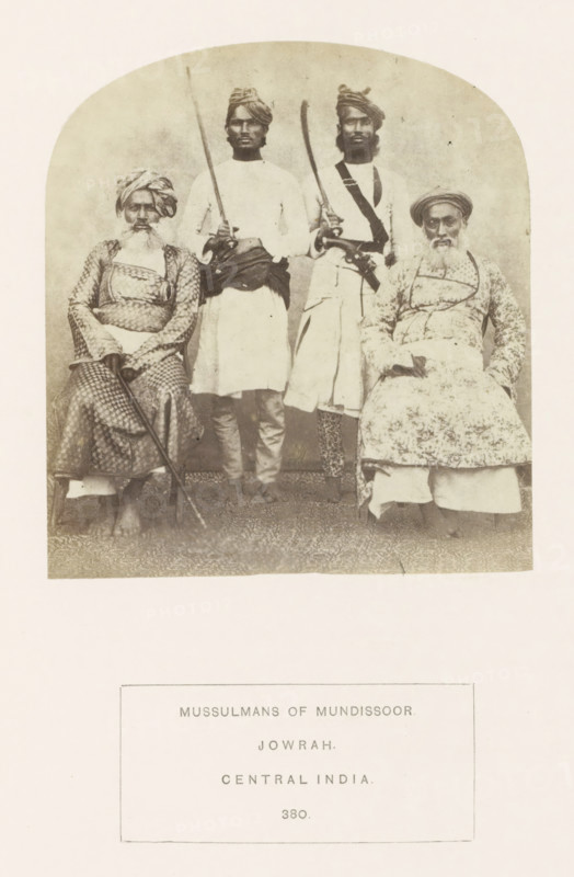 Portrait of four unknown Islamic men from Jaora, Madhya Pradesh, India, photograph, page, inscription: 'MUSSULMANS OF MUNDISOOR., JOWRAH., CENTRAL INDIA.', number: '380.', photographer: James John Waterhouse (possibly), Jaora, 1862, Central India, paper, albumen print, height 116 mm x width 106 mm, firearms: rifle, human races, peoples, nationalities, A faded black-and-white photograph shows four men posed in two seated and two standing positions within a rounded-top frame; the seated men wear patterned garments and turbans and hold long staffs or canes while the standing men wear plain tunics with sashes and turbans and hold curved blades and a long straight pole, all four displaying neutral facial expressions and facial hair, with a plain backdrop and a patterned floor beneath them.