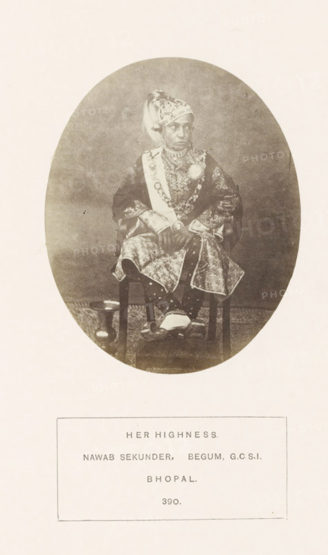 Portrait of Sekunder Begum, a queen of Bhopal, Madhya Pradesh, India, photograph, page, number: '390.', inscription: 'HER HIGHNESS., NAWAB SEKUNDER, BEGUM GCSI, BHOPAL.', photographer: James John Waterhouse (possibly), Bhopal, 1862-11, Central India, paper, albumen print, height 106 mm x width 86 mm, ruler, sovereign - BB - female ruler, human races, peoples, nationalities, An oval sepia photograph shows a seated person wearing ornate traditional clothing and jewelry, including a patterned headwrap, layered necklaces, a sash, and a brooch; the garment has intricate embroidered or patterned fabric and decorative cuffs, and the person sits with hands clasped over the lap, feet resting on a small footstool while a rounded vessel is visible on the floor beside the chair.