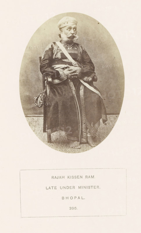 Portrait of Rajah Kissen Ram, a minister from Bhopal, Madhya Pradesh, India, photograph, page, number: '396.', inscription, q: 'RAJAH KISSEN RAM., LATE UNDER MINISTER., BHOPAL.', photographer: James John Waterhouse (possibly), Bhopal, 1862, Central India, paper, albumen print, height 102 mm x width 78 mm, human races, peoples, nationalities, ministerial council, An oval sepia photograph shows an older man seated on a wooden chair wearing a turban and a long embroidered robe with patterned trim; a sash crosses his chest and another hangs by his side, and he has a mustache and beard with hands folded over his lap; the floor beneath him has a patterned rug and his bare feet are visible.