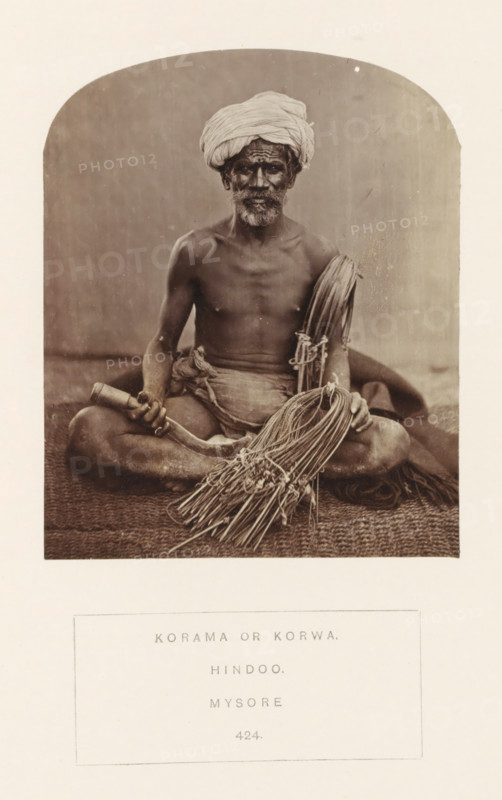 Portrait of an unknown man from the Korama community with a rope used to make a basket or a mat, Mysore, Karnataka, India, photograph, page, number: '424.', inscription: 'KORAMA OR KORWA., HINDOO., MYSORE.', c. 1865 - in or before 1875, photographer, South India, paper, albumen print, height 115 mm x width 94 mm, human races, peoples, nationalities, handicrafts and industries, A sepia-toned photograph of a seated man on a woven mat, shown from head to thighs within an arched frame; he wears a wrapped turban and has a beard and mustache, his torso is bare and he is draped in cloth around his waist; he sits cross-legged holding a curved wooden handle in one hand and a bundled collection of long thin reeds or cords in the other, with additional tied bundles resting across his lap and beside him; the background behind him is plain and softly textured.