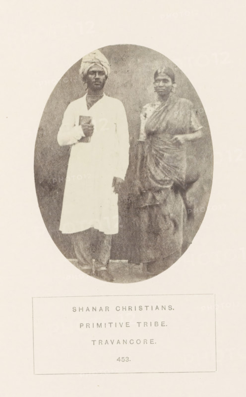 Portrait of an unknown man and woman from the Nadar community of Travancore, India, photograph, page, Travancore was a historic country in the southern tip of India. The Nadar community is also known as Shanar., inscription: 'SHAHAR CHRISTIANS., PRIMITIVE TRIBE., TRAVANCORE.', number: '453.', Travancore, c. 1865 - in or before 1875, photographer, paper, albumen print, height 103 mm x width 77 mm, human races, peoples, nationalities, An oval sepia photograph shows a man and a woman standing side by side against a plain backdrop; the man on the left wears a light long tunic and a wrapped head covering while holding a book against his chest, and the woman on the right wears a draped sari with one arm bent and her hand resting near her waist; both faces are visible and their clothing textures and folds are noticeable.