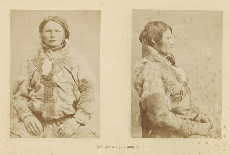 Lars Johnsen ?, d' anni 29, Two portraits of Lars Johnsen, page, Left a front view, right a side view., number: 'Tavola I.', photographer: Paolo Mantegazza, Scandinavia, photographer: Carlo Pietro Stefano Sommier, c. 1870 - in or before 1880, Paolo Mantegazza, Carlo Pietro Stefano Sommier, paper, albumen print, height 254 mm x width 340 mm, Photo in photo section at the back., fashion, clothing (fur used for clothes), adult man (side view, profile), adult man (front view), A faded sepia photograph shows two portraits of the same person mounted side by side on a light background; the left portrait is a frontal view and the right portrait is a profile view. The person has short, tousled hair and a neutral facial expression. They wear a heavy garment with a fur-trimmed collar and patched, textured fabric with visible seams and worn areas. Their hands rest in their lap, partially visible at the bottom of the left image. The photographic paper shows small spots and blemishes across the surf...