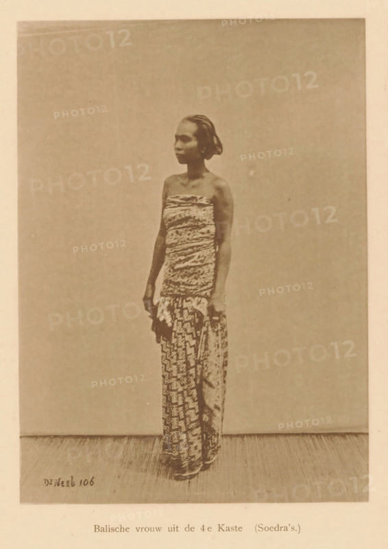Portrait of an unknown woman, Balinese woman from the 4th Caste, page, photomechanical print, maker: Christiaan Johan Neeb, c. 1892 - in or before 1897, paper, collotype, photoprint, height 121 mm x width 167 mm, historical persons, adult woman, Indonesia, A sepia-toned photograph of a woman standing in front of a plain backdrop, shown full length and facing slightly to the side, wearing a strapless wrapped bodice and a patterned wrap skirt that reaches the floor, with her hair pulled back and her arms relaxed at her sides.