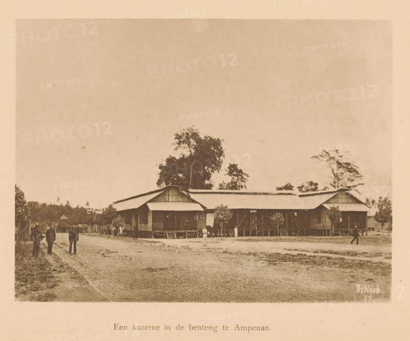 View of a barracks in Ampenan, A barracks in the benteng in Ampenan, page, photomechanical print, maker: Christiaan Johan Neeb, c. 1892 - in or before 1897, paper, collotype, photoprint, height 120 mm x width 158 mm, other dwelling types, Lombok, Ampenan, A sepia photograph showing a large wooden building with a corrugated roof elevated on stilts, a covered veranda, and steps leading up to entrances, set behind a dirt foreground; several trees rise behind and beside the building, and small shrubs or potted plants line the veranda; scattered people stand or walk in front of and near the building, and a faint pair of tracks run across the left side of the ground.