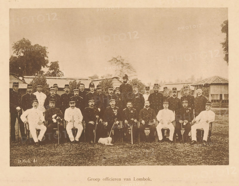 Group portrait of officers of Lombok, Group of officers of Lombok, page, photomechanical print, maker: Christiaan Johan Neeb, c. 1892 - in or before 1897, paper, collotype, photoprint, height 119 mm x width 165 mm, anonymous historical persons depicted in a group, in a group-portrait, ranks (in the army, navy, air force), A sepia-toned group portrait of uniformed men arranged in rows outdoors, with seated figures in front and standing figures behind, many wearing dark military-style coats and peaked caps while a few wear lighter uniforms; a small dog lies on the ground in front of the seated row; trees and simple buildings with thatched or sloped roofs are visible in the background under a wide sky.