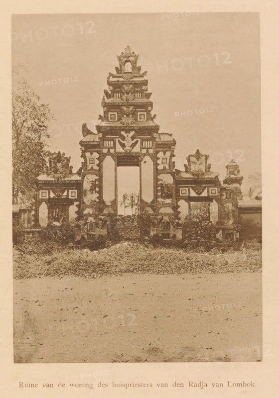 Ruin of the house of the house priest of the Raja of Lombok, View of ruins of the house of a house priest of the Raja of Lombok, page, photomechanical print, maker: Christiaan Johan Neeb, c. 1892 - in or before 1897, paper, collotype, photoprint, height 164 mm x width 116 mm, ruin of a building, architecture, Indonesia, An aged photograph shows a carved stone gateway with a central tall opening flanked by smaller openings, topped by layered ornamental tiers with sculpted motifs and decorative reliefs, standing on a grassy mound with scattered stones; low ornamental walls and sculpted pedestals extend to either side, and trees are visible behind and beside the structure, while the foreground shows a bare expanse of ground leading up to the mound.