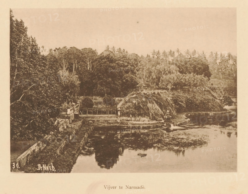 View of a water at Narmada, Pond at Narmade, page, photomechanical print, maker: Christiaan Johan Neeb, c. 1892 - in or before 1897, paper, collotype, photoprint, height 121 mm x width 167 mm, landscapes with waters, waterscapes, seascapes (in the temperate zone), Lombok, Narmada, A sepia-toned photograph shows a landscape with dense trees and tall palms along the upper portion, a thatched mound and a small pavilion near the center, a stone wall and a bridge-like structure extending across a water body, and a calm reflective pond in the foreground bordered by vegetation.