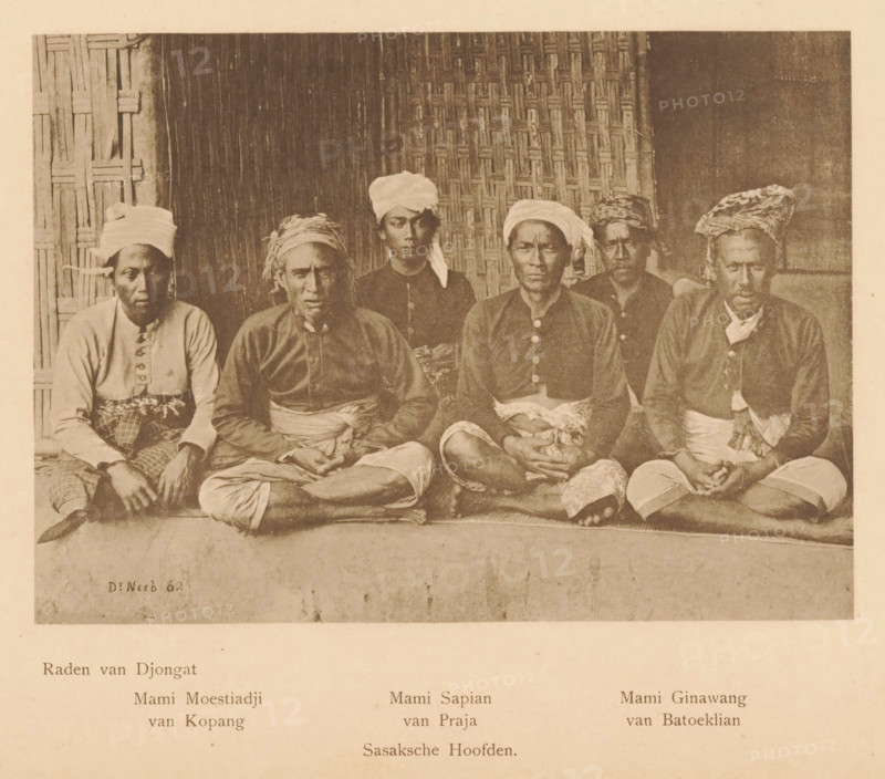 Portrait of six men including Raden van Djongat, Mami Moestiadji van Kopang, Mami Sapian van Praja and Mami Ginawang van Batoeklian, Sasaksche Hoofden, page, photomechanical print, maker: Christiaan Johan Neeb, c. 1892 - in or before 1897, paper, collotype, photoprint, height 120 mm x width 167 mm, historical persons, adult man, Indonesia, A sepia-toned photograph showing a group of six seated men in traditional clothing arranged in two rows against a woven and wooden backdrop; the men in the front row sit cross-legged with hands resting on their laps and wear buttoned shirts and patterned lower garments with sashes, while the men in the back row sit or stand slightly higher and wear headwraps and darker tops; the backdrop alternates between a vertical wooden panel on one side, a woven mat in the center, and a darker plain surface on the other side; the floor area in front of them appears as a raised platform with a textured edge and the overall image has an aged, grainy appearance.