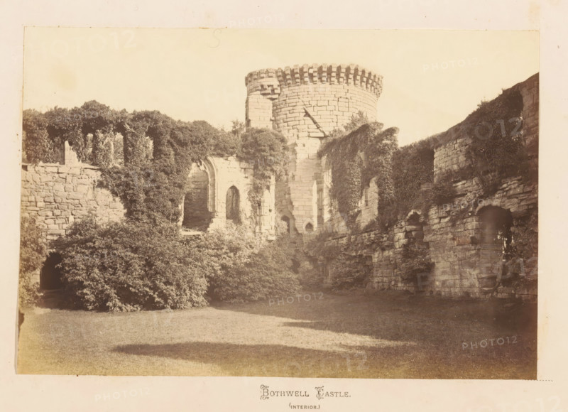 Bothwell Castle (interior), View of Bothwell Castle, photograph, page, South Lanarkshire, c. 1862 - in or before 1867, photographer, paper, albumen print, height 120 mm x width 179 mm, landscape with tower or castle, castle, A sepia-toned photograph of a stone castle interior showing a tall round tower with a crenellated top and a cylindrical stone face, flanked by ruined stone walls with arched openings and window-like recesses; portions of the walls are covered in dense ivy and climbing plants that cascade down and obscure sections of the masonry, while shrubs and bushes grow at the base of the ruins; a grassy foreground stretches toward the stone structures, and patches of shadow fall across the lawn.