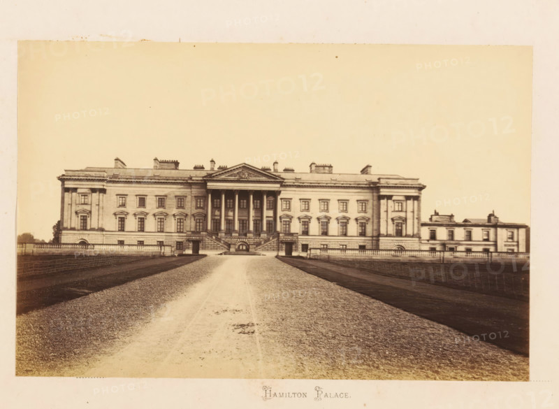 View of Hamilton Palace, Hamilton Palace, photograph, page, Lanarkshire, c. 1862 - in or before 1867, photographer, paper, albumen print, height 116 mm x width 178 mm, country-house, A large neoclassical building viewed from the front with a central portico supported by tall columns and a triangular pediment, flanked by symmetrical wings with rows of evenly spaced windows and decorative window surrounds, stone balustrades and staircases leading up to the main entrance, a wide gravel driveway running toward the building between darker planted or turfed areas, low fencing along the sides of the driveway, and a pale sky occupying the upper portion of the image.