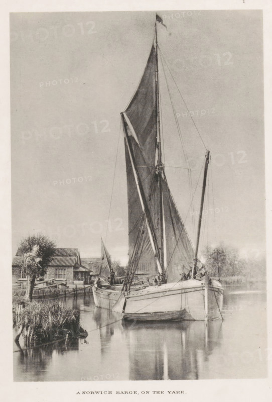 A Norwich barge, on the yare, Barge with two men, page, photomechanical print, photographer: John Payne Jennings, Norfolk Broads, cliché maker: Permanent Photo Printing Works, Ashtead, Surrey, c. 1886 - in or before 1891, paper, collotype, photoprint, height 167 mm x width 115 mm, Print opposite title page., sailing-ship, sailing-boat, river, landscapes with waters, waterscapes, seascapes (in the temperate zone), A tall sailboat with its sails partially unfurled is moored on calm water, its masts and rigging rising high into the sky with a small flag at the top. The boat's hull sits low in the water and a smaller rowboat is tied alongside it. Reflections of the masts and hull appear on the smooth surface of the water. Along the shoreline there is a cluster of buildings with pitched roofs, a tree with textured foliage, and patches of reeds and grass at the water's edge. The image is rendered in a monochrome tone with a soft, evenly lit sky occupying much of the background.