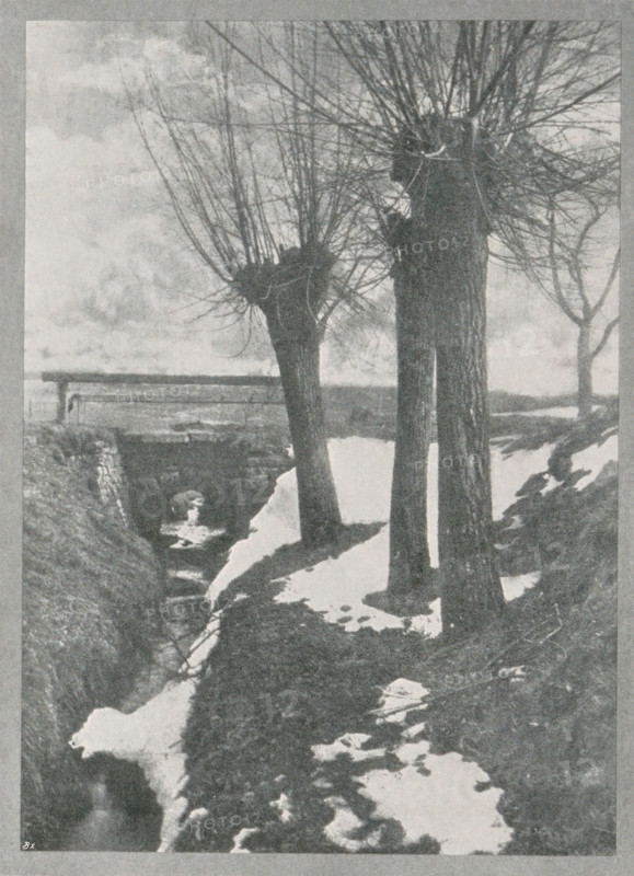 Landscape with snow, Letzter schnee, page, photomechanical print, inscription: 'Photographische Mitteilungen LX', monogram: 'BX', photographer: Carl Winkel, cliché maker: unknown, c. 1898 - in or before 1903, paper, autotypie, height 95 mm x width 124 mm, landscapes, snow, A grayscale scene showing a narrow stream running between banks with patches of snow along the ground, several tall trees with thick trunks and dense, pruned upper branches standing beside the stream, a simple wooden bridge crossing the stream in the middle distance, bare branches of other trees visible against a cloudy sky, and uneven terrain with exposed soil and snow along the water’s edge.