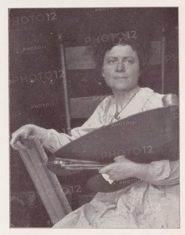 Portrait of an unknown woman, Bildnis der Mrs. K., page, photomechanical print, inscription: 'Photographische Mitteilungen XL', monogram: 'MR&C', photographer: Gertrude Käsebier, New York (city), cliché maker: Meisenbach, Riffarth & Cie., c. 1898 - in or before 1903, North America, paper, autotype, height 169 mm x width 130 mm, historical persons - BB - woman, A seated person with short curly hair looks slightly to the side while holding a dark oval object and a stack of flat rectangular items; the person wears a light-colored garment with a visible neckline and a beaded necklace, and one hand rests on the back of a wooden chair; the background shows vertical and horizontal rectangular shapes and a dark area above.