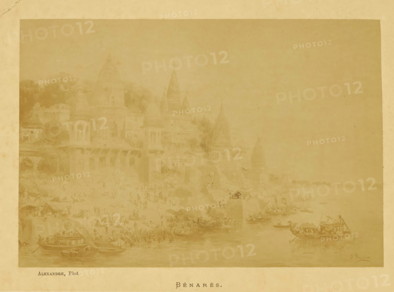 Bénarès, Photo reproduction of Bénarès by Jean Baptiste Robie, photograph, reproduction, page, photographer: Alexandre, after painting by Jean Baptiste Robie, c. 1880 - in or before 1885, paper, albumen print, height 128 mm x width 187 mm, Photo opposite title page, behind cover., prospect of city, town panorama, silhouette of city, A faded sepia-toned scene shows a riverside with multiple small boats on the water and crowds of tiny indistinct figures along the shore, with larger boat structures visible in the foreground; behind the shoreline a series of temple-like buildings with domes and spires rise amid indistinct trees and architectural forms, and the whole image is bordered by a lighter margin.