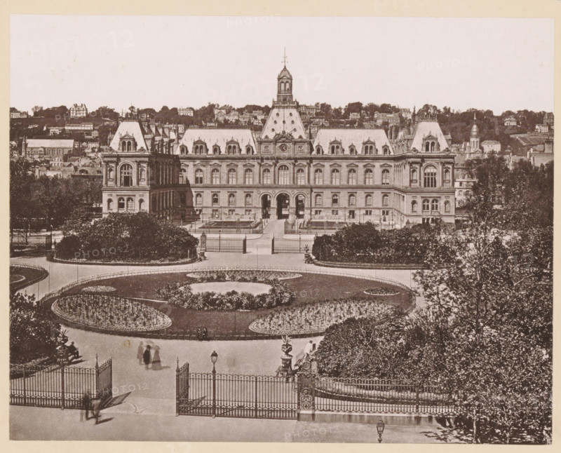Le Havre, L'Hôtel-de-Ville, View of the town hall of Le Havre, page, photomechanical print, inscription: 'Journal le Nord Contemporain, No 32, année 1883.', inscription: 'Le Nord Contemporain, Revue Artistique & Archéologique', photographer: NC, cliché maker: NC, c. 1878 - in or before 1883-05-05, NC, photographer, cliché maker, paper, collotype, photoprint, height 172 mm x width 219 mm, Print on fifth unnumbered page after page 128., prospect of city, town panorama, silhouette of city, townhall, A wide view of a grand stone building with a central tower and symmetrical wings, featuring steep slate roofs with dormer windows and ornate architectural details, stands behind an ornate wrought iron gate and formal gardens with curved flowerbeds, trimmed hedges, and pathways; trees flank the scene and a few blurred figures and a carriage appear near the entrance area, while a hillside dotted with houses and additional buildings rises behind the main structure.