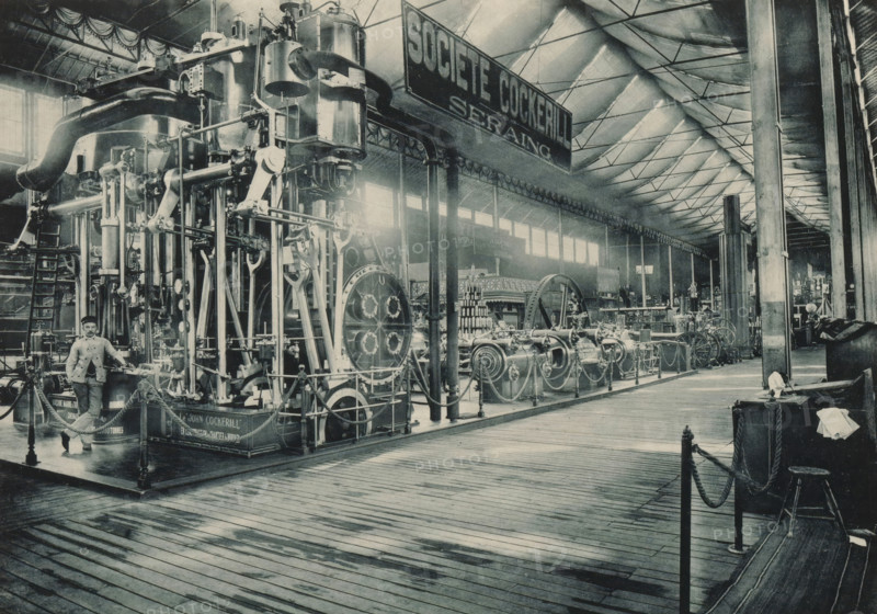 Société John Cockerill Seraing, View of a setup of Société Anonyme John Cockerill from Seraing at the Antwerp World Exhibition in 1894, Exposition Universelle d'Anvers 1894, page, photomechanical print, photographer: Charles Bernhoeft, Antwerp, cliché maker: Charles Bernhoeft, Luxembourg (Belgian province), 1894, Charles Bernhoeft, photographer, cliché maker, paper, collotype, photoprint, height 153 mm x width 216 mm, industries, metal, world fair, world exhibition, machines, parts of machines, tools and appliances, World Exhibition 1894 (Antwerp), Period, 1894-05-05 - 1894-11-05, A large indoor exhibition space with a high pitched ceiling supported by metal trusses and tall columns, a long wooden plank floor in the foreground, and an extensive display of heavy industrial machinery occupying the left and center areas. The machinery includes tall vertical cylinders, large flywheels, connecting rods, pipes, valves, chains, and ornate metal frameworks mounted on raised platforms with rope...