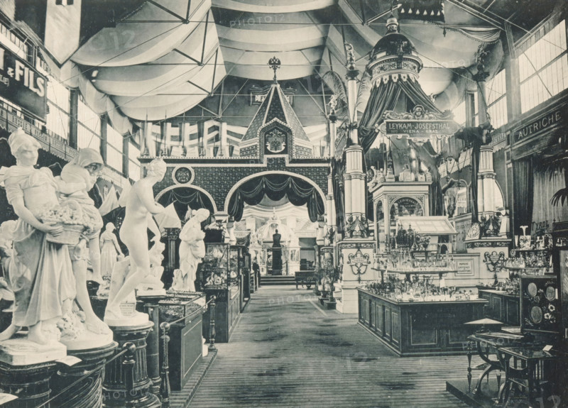 View of the Italian, Russian and Austrian parts of the main exhibition of the Antwerp World's Fair in 1894, Coup d'oeil sur les Sections, Italienne Russe Autrichienne, Exposition Universelle d'Anvers 1894, page, photomechanical print, photographer: Charles Bernhoeft, Antwerp, cliché maker: Charles Bernhoeft, Luxembourg (Belgian province), 1894, Charles Bernhoeft, photographer, cliché maker, paper, collotype, photoprint, height 153 mm x width 216 mm, Print on third unnumbered page after page 34., piece of sculpture, reproduction of a piece of sculpture, world fair, world exhibition, World Exhibition 1894 (Antwerp), Period, 1894-05-05 - 1894-11-05, A large indoor exhibition hall filled with sculpted figures and ornate architectural displays under a vaulted fabric ceiling, showing rows of marble statues on pedestals in the foreground and decorative columns, draped canopies, and a domed pavilion toward the center and right; tall windows line the side walls, decorative friezes and patterned...