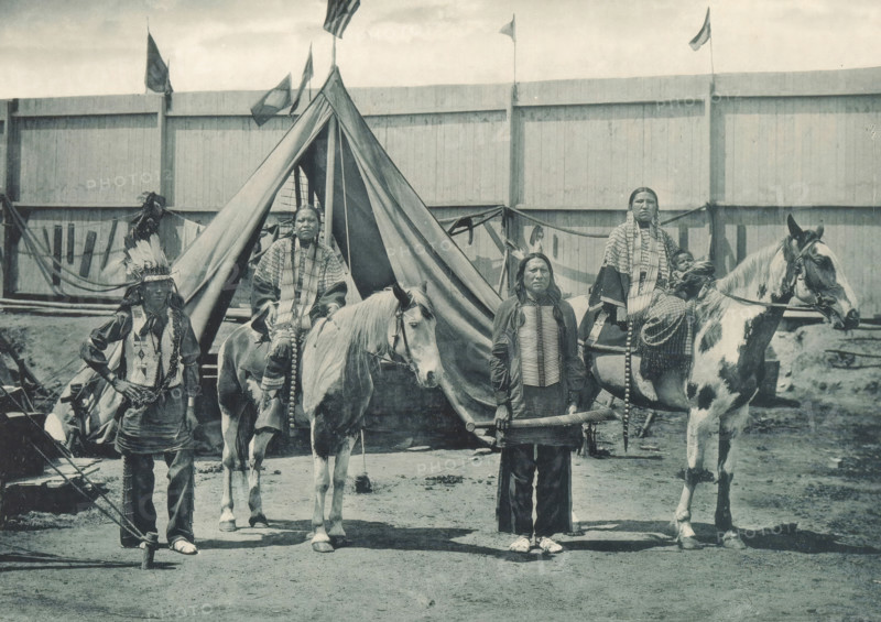 Members of Pawnee Bill's group at the Antwerp World Exhibition in 1894, Types de la Troupe de Pawne Bill, Chefs Jouws avec leurs femmes, Exposition Universelle d'Anvers 1894, page, photomechanical print, photographer: Charles Bernhoeft, Antwerp, Luxembourg (Belgian province), 1894, paper, collotype, photoprint, height 153 mm x width 216 mm, Print on third unnumbered page after page 62., horse, indigenous peoples of North America, world fair, world exhibition, World Exhibition 1894 (Antwerp), Period, 1894-05-05 - 1894-11-05, A group of people posed in front of a tent with a tall triangular entrance and a wooden fence behind it; two horses stand near the tent, one light-colored and one with darker patches, both wearing bridles and saddles; several adults wear patterned clothing and long braided hair, one person standing in front holding a cylindrical object, another wearing a feathered headdress, and one seated on a horse holding a child wrapped in cloth; flags fly above the fence and fa...