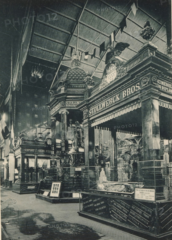 View of the food section of the Belgian part of the Antwerp World Exhibition in 1894, Section Belge, Groupe de l'Alimentation, Exposition Universelle d'Anvers 1894, page, photomechanical print, photographer: Charles Bernhoeft, Antwerp, Luxembourg (Belgian province), 1894, paper, collotype, photogravure, height 215 mm x width 152 mm, Print on third unnumbered page after page 114., counter, shop, industries, food, drink, stimulants, world fair, world exhibition, World Exhibition 1894 (Antwerp), Period, 1894-05-05 - 1894-11-05, A large indoor scene shows ornate exhibition booths with heavy decorative architecture, domed and columned structures, sculpted figures, and carved ornamentation; a prominent canopy with fringe hangs over one display and an eagle sculpture sits atop a decorated crest; flags hang from the high rafters of a vaulted ceiling and small pennants drape across the upper space; glass display cases contain objects and are set on raised platforms while framed items rest on ea...