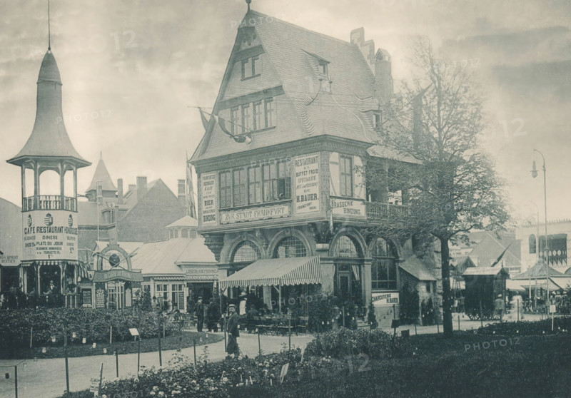 Zur Stadt Frankfurt, View of a reconstructed part of Frankfurt at the Antwerp World Exhibition in 1894, Exposition Universelle d'Anvers 1894, page, photomechanical print, photographer: Charles Bernhoeft, Antwerp, cliché maker: Charles Bernhoeft, Luxembourg (Belgian province), 1894, Charles Bernhoeft, photographer, cliché maker, paper, collotype, photoprint, height 153 mm x width 217 mm, Print on third unnumbered page after page 18., restaurant, civic architecture, edifices, dwellings, world fair, world exhibition, World Exhibition 1894 (Antwerp), Period, 1894-05-05 - 1894-11-05, A streetscape showing a large multi-story building with a steeply pitched roof and decorative timber framing, adjacent to a tower with a conical roof and open upper pavilion, a row of awnings and outdoor seating in front, several people standing and sitting near the entrance and under the awnings, ornamental windows and arched openings on the ground level, trees with bare branches beside the building, a lamp po...