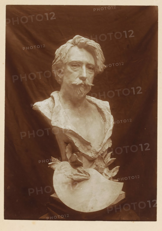 Bust of Willem Linnig, photograph, page, photographer: Alexandre van Antro, c. 1891 - in or before 1896, paper, daylight collodion silver print, height 171 mm x width 121 mm, Person, Willem Linnig (II), piece of sculpture, reproduction of a piece of sculpture, historical persons not known by name, A sculpted bust of a man with wavy hair, a moustache, and a small beard is shown against a dark draped background, the figure wearing an open-collared garment with textured folds and a partially exposed chest, and the sculpture continues downward into a decorative base featuring large stylized leaves and a curved shield-like element.