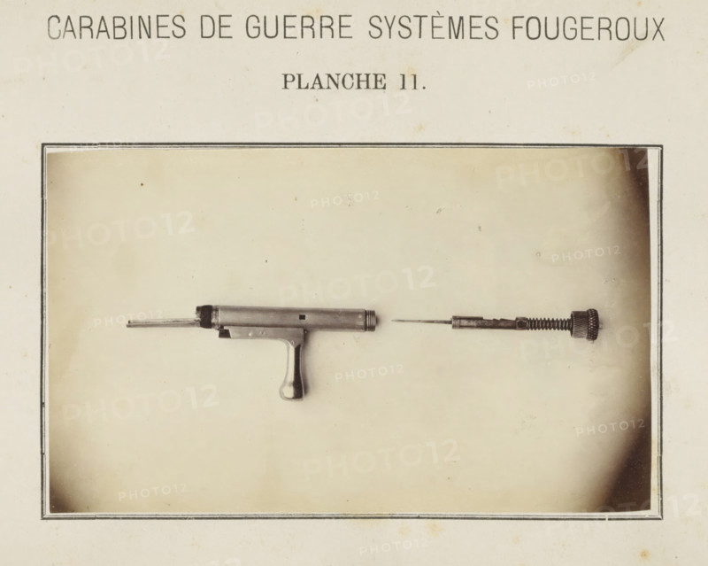 Safety catch of a rifle in two parts, photograph, page, number: 'Planche 11.', inscription: 'Carabines de guerres systèmes Fougeroux', photographer: Edouard Magis, Liège, c. 1857 - in or before 1867, paper, albumen print, height 158 mm x width 96 mm, Image in section at the back., firearms: rifle, A faded photograph shows a disassembled metallic tool or firearm component mounted against a light, aged background with a thin dark border. The left piece resembles a short cylindrical barrel with a protruding rod and a small squared opening, attached to a grip with a rounded handle. The right piece consists of a slender rod attached to a textured cylindrical cap and a spring-like section, aligned horizontally opposite the left component. The background has subtle stains and small spotting, and a rectangular frame surrounds the central image.